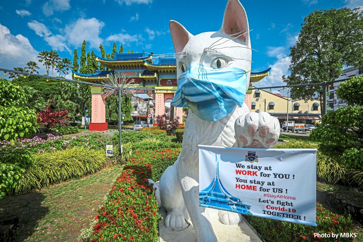 The White Cat statue at Padungan in Kuching wearing a face mask and holding a banner from the Kuching South City Council reminding the public to stay at home. - ZULAZHAR SHEBLEE / THE STAR